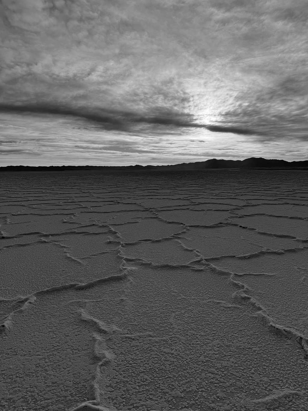 Cracked salt crust of a lithium salar stretching to a mountain range at sunset.